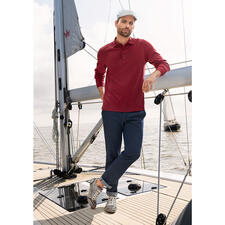 Rouge brique Mann in rotem Pima Interlock Polo Shirt steht auf einem Boot, lächelt.