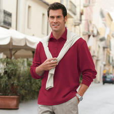 Rouge brique Mann in rotem Pima Interlock Polo Shirt steht in einer Stadt, freundlich lächelnd.