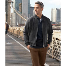 Marine Mann in schwarzem Pima-Interlock-Poloshirt, steht in einer natürlichen Umgebung mit Bergen im Hintergrund.