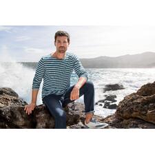 Manches longues, Jean/Écru Mann im gestreiften Langarmshirt sitzt an einem Felsen am Meer.