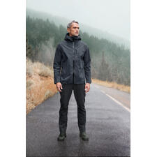 Herren, Jacke und Hose Mann in grauer Hardshell-Jacke steht auf nasser Straße in bewaldeter Landschaft.