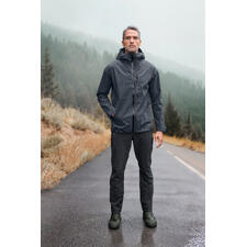 Herren, Jacke und Hose Mann in grauer Hardshell-Jacke steht auf nasser Straße, im Hintergrund Berge.