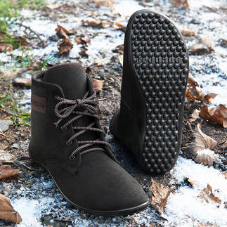 Schwarze Schnür-Boots mit flexibler Sohle und Schnürsenkeln auf einem Waldweg.