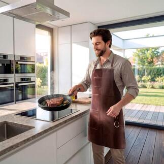 Mann mit Büffelleder-Grillschürze kocht in einer modernen Küche.