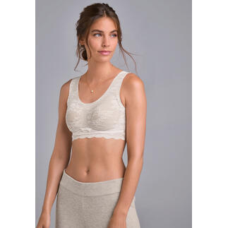 Frau in cremefarbenem Spitzen-Bralette, lächelt vor einem neutralen Hintergrund.
