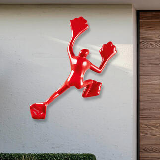 Rotere Skulptur an einer hellen Wand im Außenbereich.