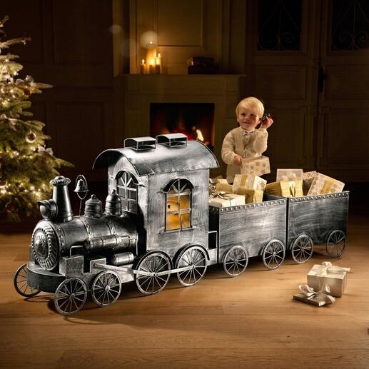 Nostalgie-Zug aus Metall mit Geschenken, im Hintergrund ein dekorierter Weihnachtsbaum.