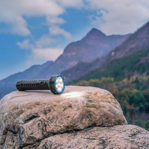 Bidirektionale 5.000 Lumen Taschenlampe auf einem Stein mit Berglandschaft im Hintergrund.