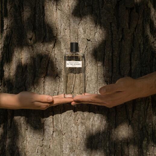 Flasche In the Woods Eau de Parfum in Händen, vor einem Baumstamm.
