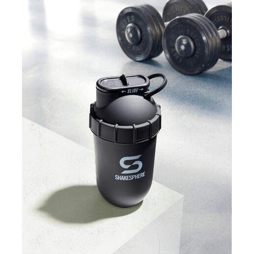 Dieser Fitness-Shaker nutzt allein die in der abgerundeten Kapselform entstehende Zentrifugalkraft – ohne Ecken, in denen sich Pulverrückstände festsetzen können. Schwarzer Shaker auf einer weißen Oberfläche mit Hanteln im Hintergrund.
