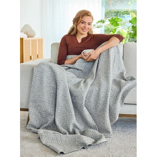 Idéale également comme couverture légère pour des heures douillettes sur le canapé. Frau sitzt auf einem Sofa mit einer jacquard Decke umhüllt.