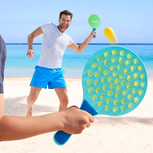 Mann spielt am Strand mit einem ovalen Schlagspiel und trifft den Ball.