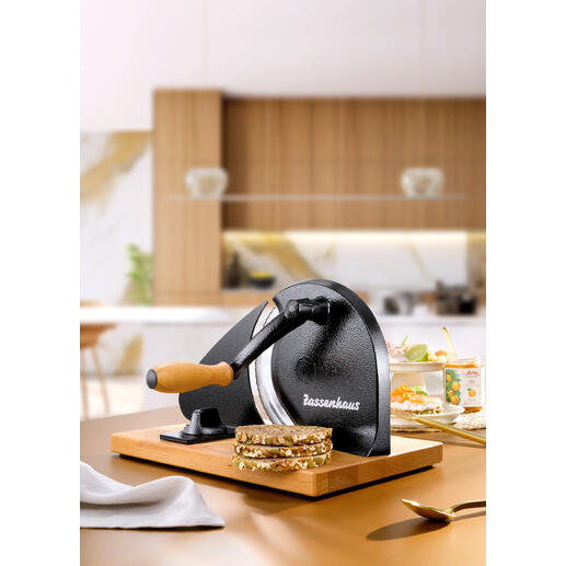 Handkurbel-Brotschneider auf einer Holzplatte mit frisch geschnittenem Brot.