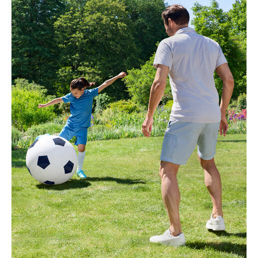 Ein Junge spielt mit einem übergroßen Fußball im Garten.