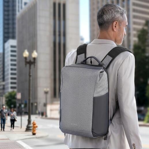 Mann mit grauem Anti-Diebstahl-Rucksack auf dem Rücken vor urbanem Hintergrund.