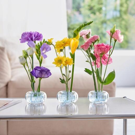 Drei Mini-Steckvasen mit bunten Blumen auf einem Tisch.