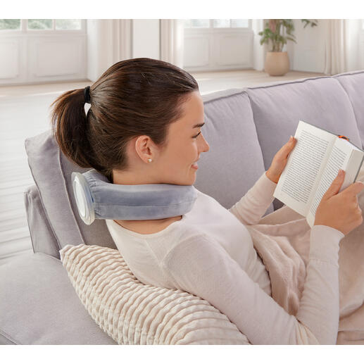 Frau mit Nackenwärmer liest ein Buch auf einem Sofa