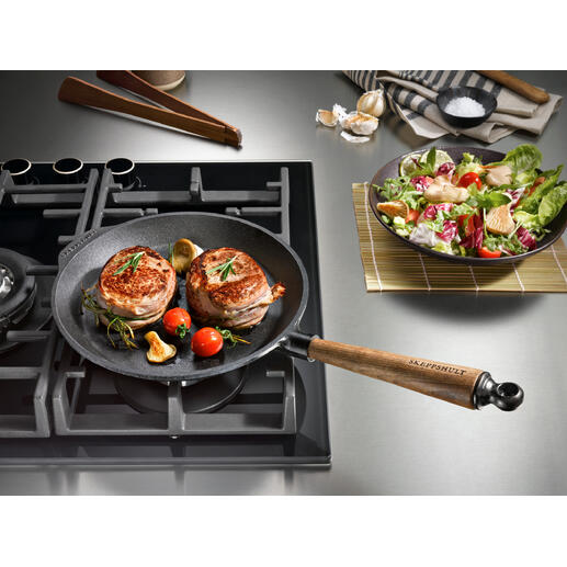 Gusseisenpfanne auf Kochfeld mit gebratenem Fleisch und Gemüse