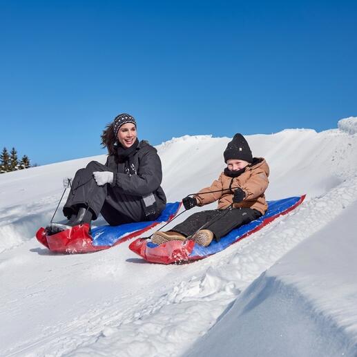 Frau und Kind fahren mit XL-Schneegleitern einen Schneehang hinunter.
