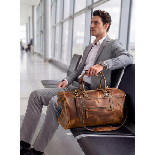 Mann sitzt am Flughafen mit Büffelleder-Weekender neben sich.