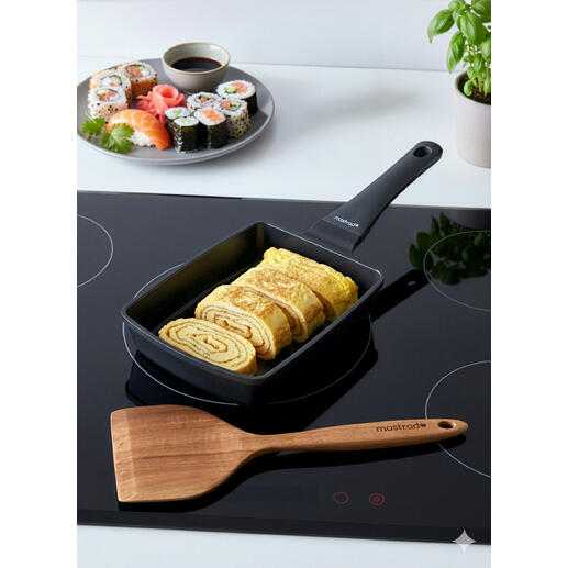 Tamagoyaki-Pfanne mit gefalteten Eiern neben Sushi-Platte.