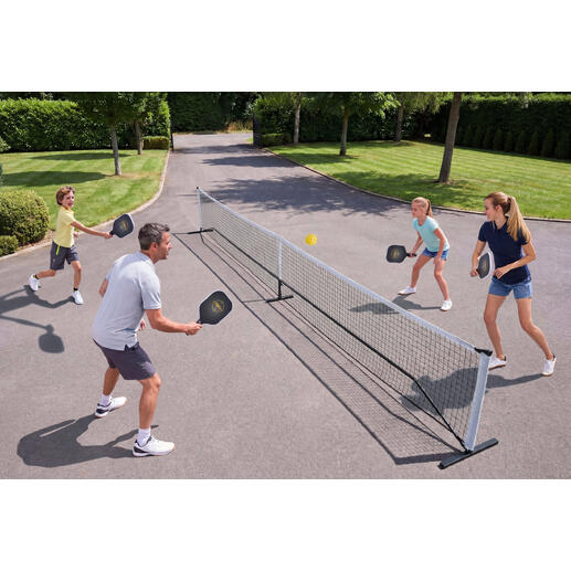 Familie spielt Pickleball im Freien, mit Netz und Bällen.