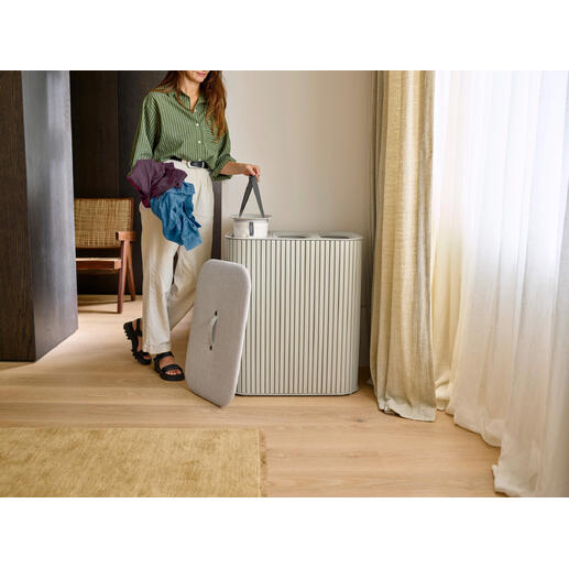 Frau mit bunten Kleidungsstücken steht neben einem Wäschesammler.