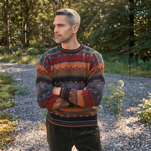 Mann in buntem Pullover steht in einer grünen Umgebung.