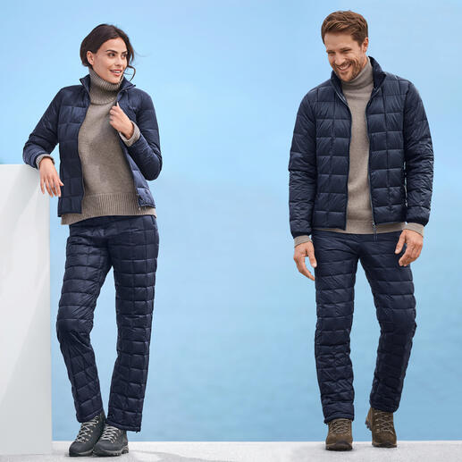 Mann und Frau in Taion Daunenjacke und -hose, beide in dunkelblau, vor blauem Hintergrund.