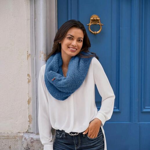 Frau trägt weißen Bluse mit blauem Bouclé-Poncho vor einer blauen Wand