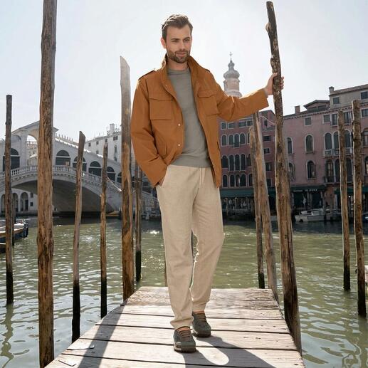 Mann steht auf einem Steg am Wasser, trägt eine Jacke und Sneaker.