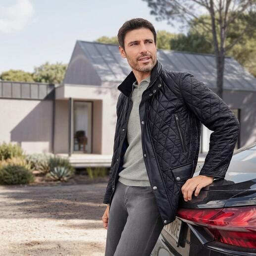 Mann in schwarzer Steppjacke mit Lammnappa vor einem modernen Gebäude.