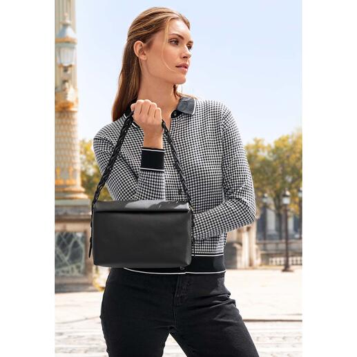 Frau mit einer schwarzen Handtasche posiert vor einer Stadtlandschaft.