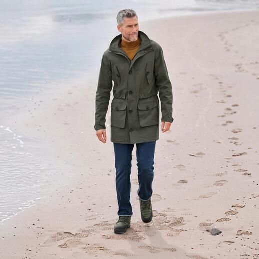 Mann in grünem Baumwollpark mit Taschen, der am Strand entlang läuft.