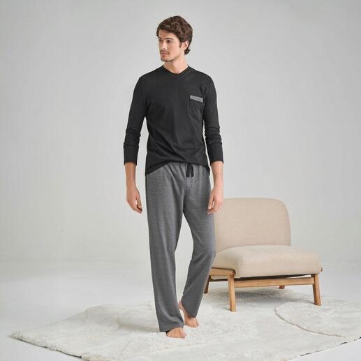 Mann in schwarzem Langarmshirt und grauen Pyjamahosen steht auf einem Teppich.