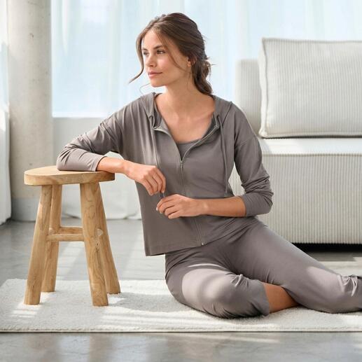 Frau sitzt in eleganter Loungewear-Kombination auf einem Teppich.