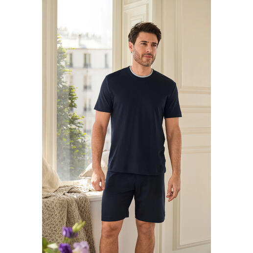 Recovery Pyjama Mann steht in einem hellen Raum in einem navy-farbenen Recovery-Pyjama mit kurzen Hosen.