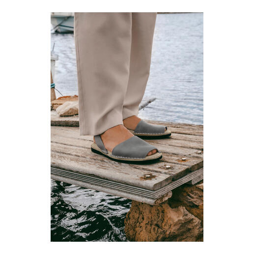 Avarcas de Menorca Person mit grauen Avarcas de Menorca auf Holzsteeg, über dem Wasser.