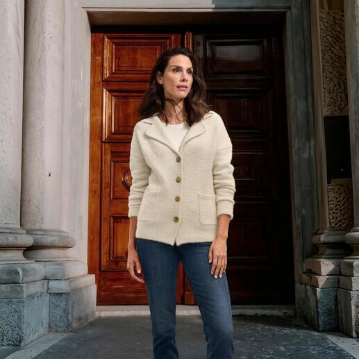 Frau trägt einen flauschigen Strickblazer in Ecru vor einer hölzernen Tür.