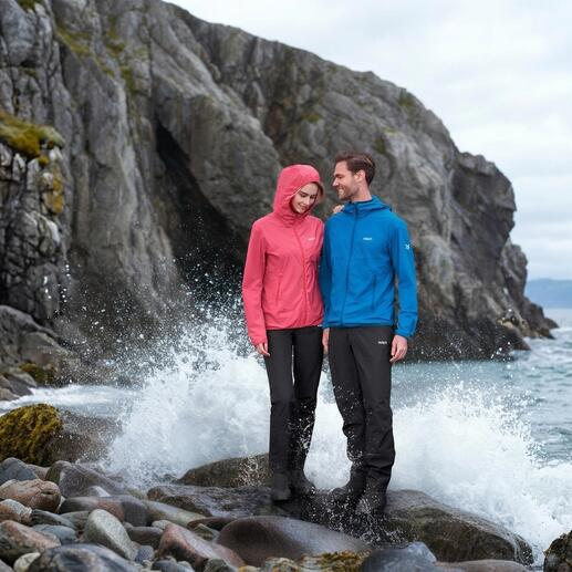 Paar in Outdoor-Bekleidung, eine Person trägt pinke Softshelljacke, andere in blauer Jacke neben stürmischem Wasser.