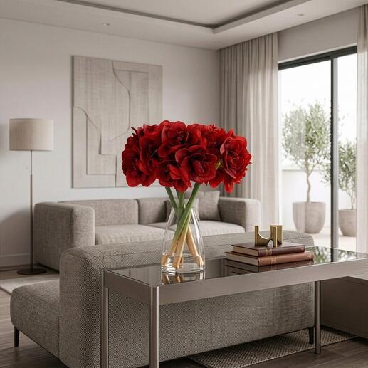 Fülliger Amaryllisstrauß in einer Vase auf einem Glastisch mit Sofa im Hintergrund.