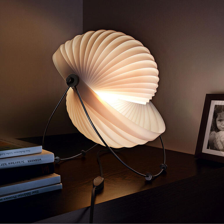 Design-Leuchte 'Eclipse' mit geschwungener, blütenblattähnlicher Lampe auf einem Tisch.