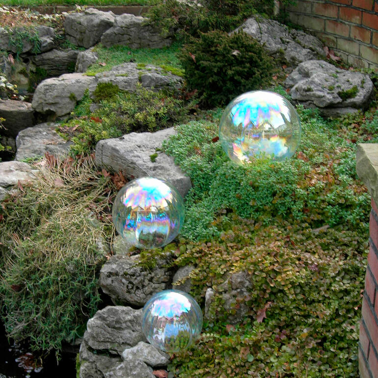 Wie echte Seifenblasen reflektieren diese Kugeln das einfallende Licht. Drei große Seifenblasen auf grünem Moos zwischen Steinen