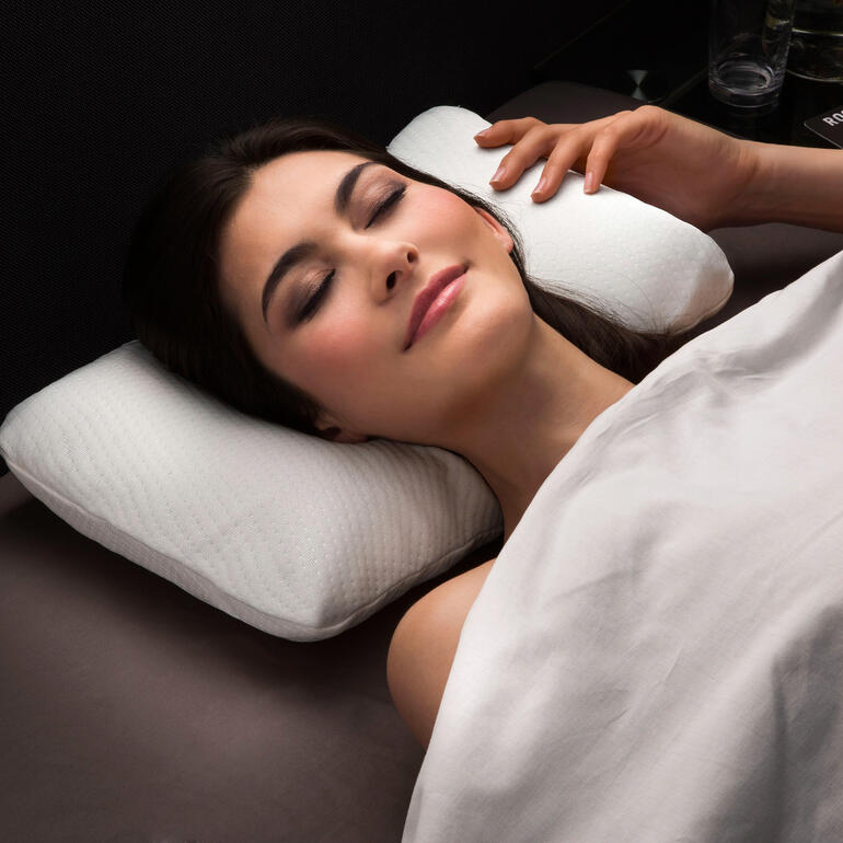 Frau entspannt mit zwei Visco-Cool-Reisekissen in einem Bett.