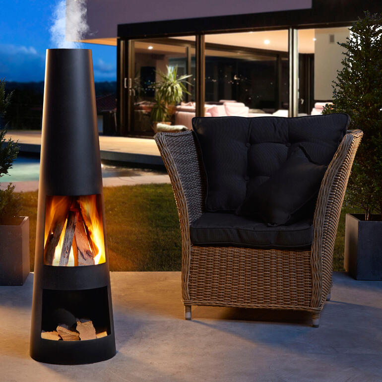 Moderne Terrassenkamin mit brennendem Holz neben einem gemütlichen Sessel.