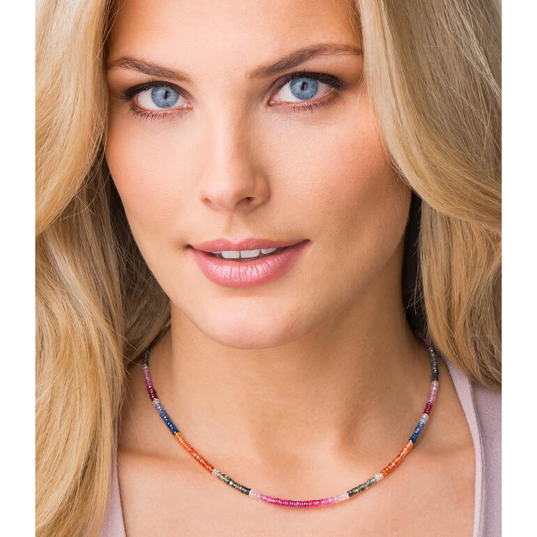 Collier de saphirs Frau mit Saphir-Kette, lächelnd im Freien, umgeben von Pflanzen.