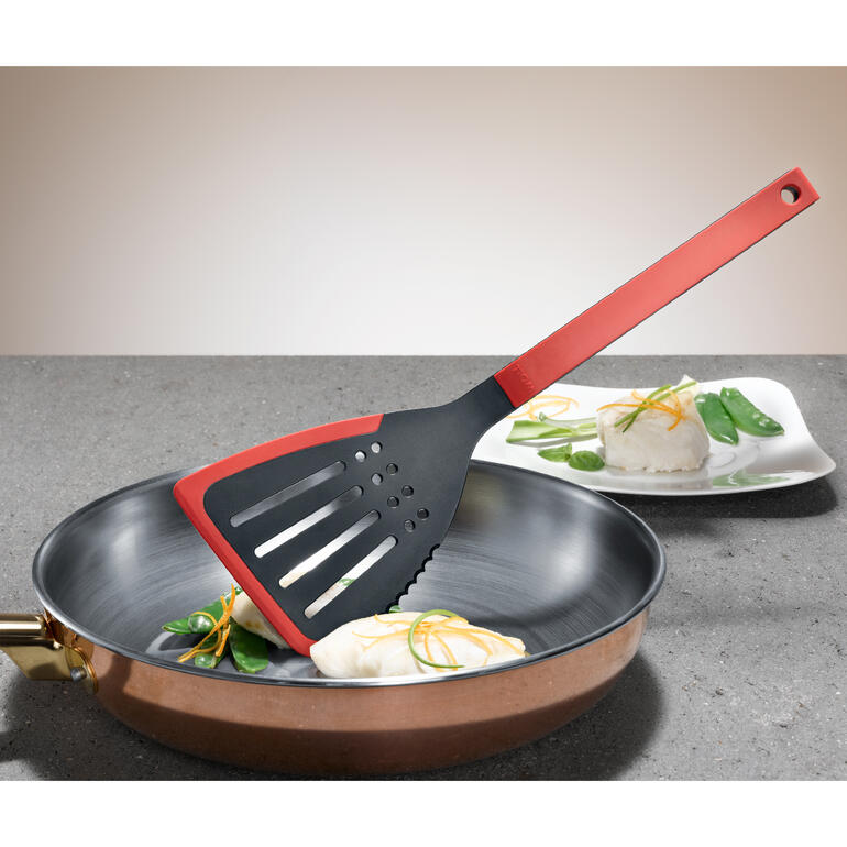 Pfannenwender „Flip it“ liegt neben einem Fischfilet in einer Pfanne.
