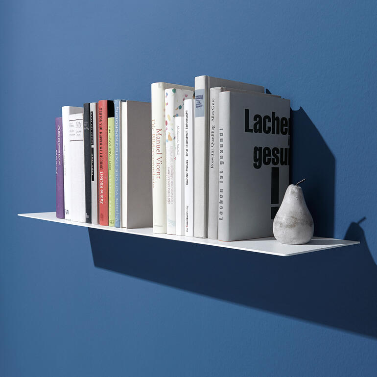 Weißes Wandregal mit mehreren Bücher auf blauer Wand