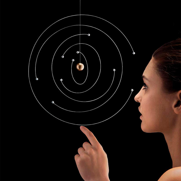 Frau zeigt auf ein schwebendes Atommodell mit Kugeln und spiralförmigen Bahnen.