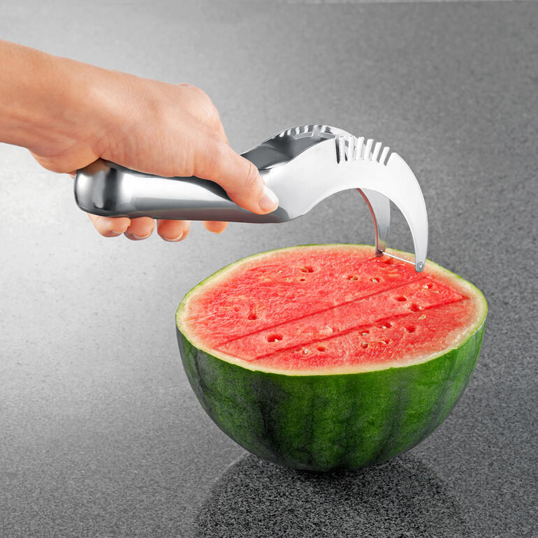 Hand mit Melonenschneider, der in eine halbierte Wassermelone führt.